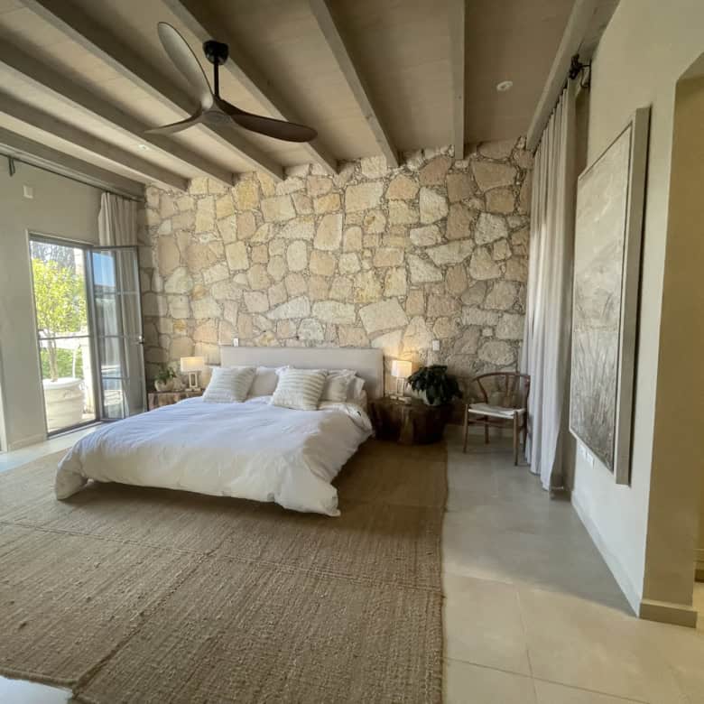 Bedroom with stone wall, large bed, and balcony doors for natural light.