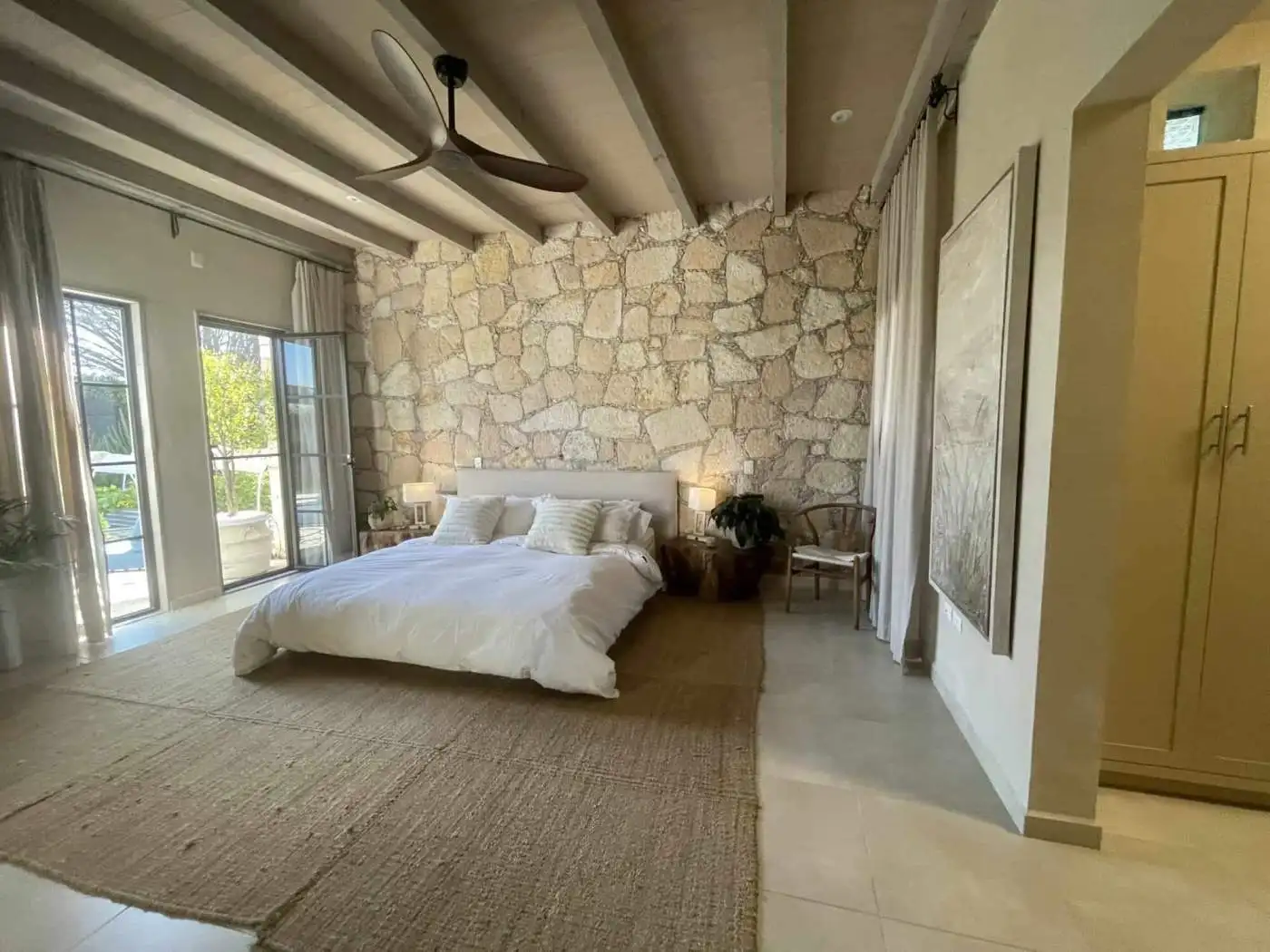 Bedroom with stone wall, large bed, and balcony doors for natural light.