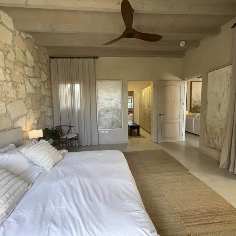 Modern rustic bedroom with stone wall, large windows, and cozy decor.