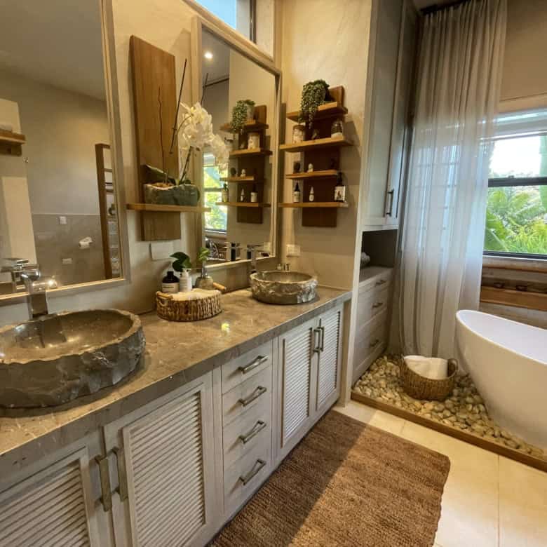 Elegant bathroom with stone sinks and a relaxing bathtub near large windows.