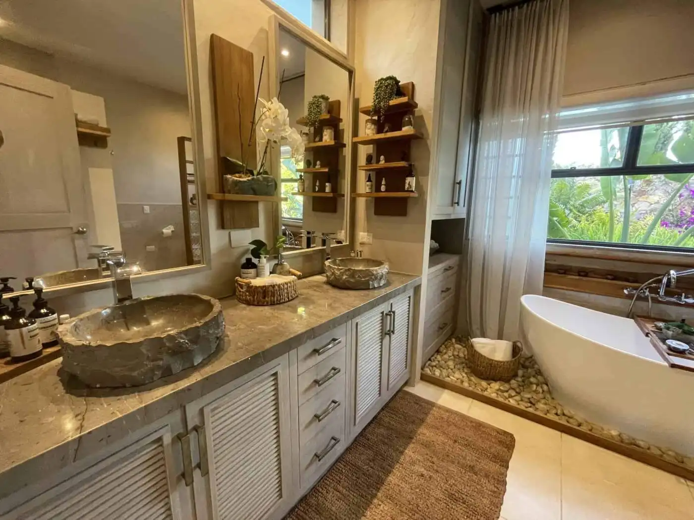 Elegant bathroom with stone sinks and a relaxing bathtub near large windows.