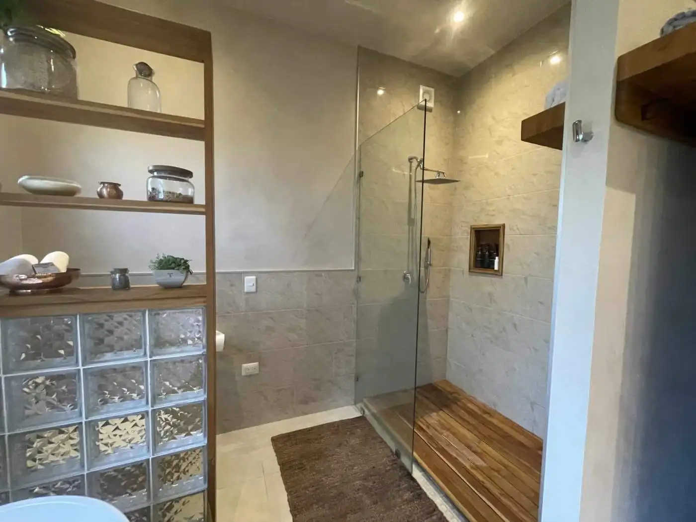 Modern bathroom with walk-in shower, glass partition, and wooden flooring accents.