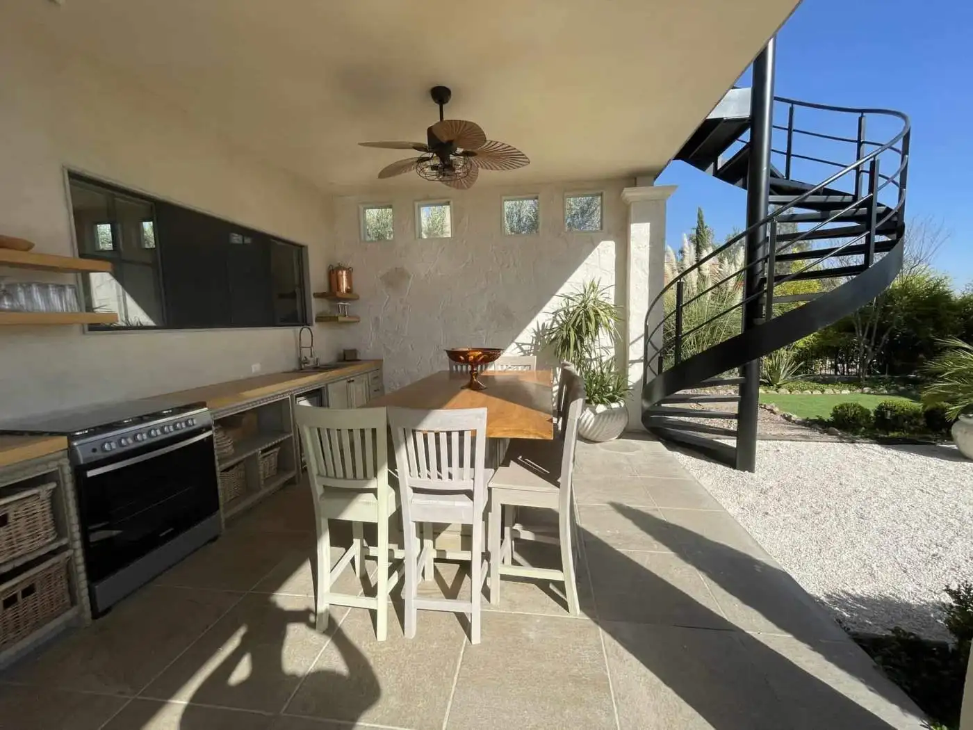 Outdoor kitchen with dining table and spiral staircase in a contemporary home.