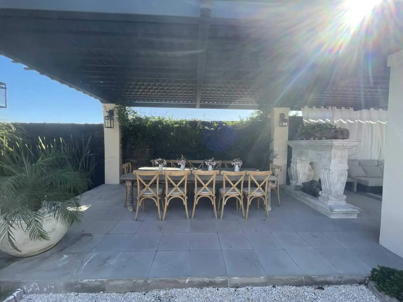 Outdoor dining space with shaded patio, stylish furniture, and lush greenery backdrop.