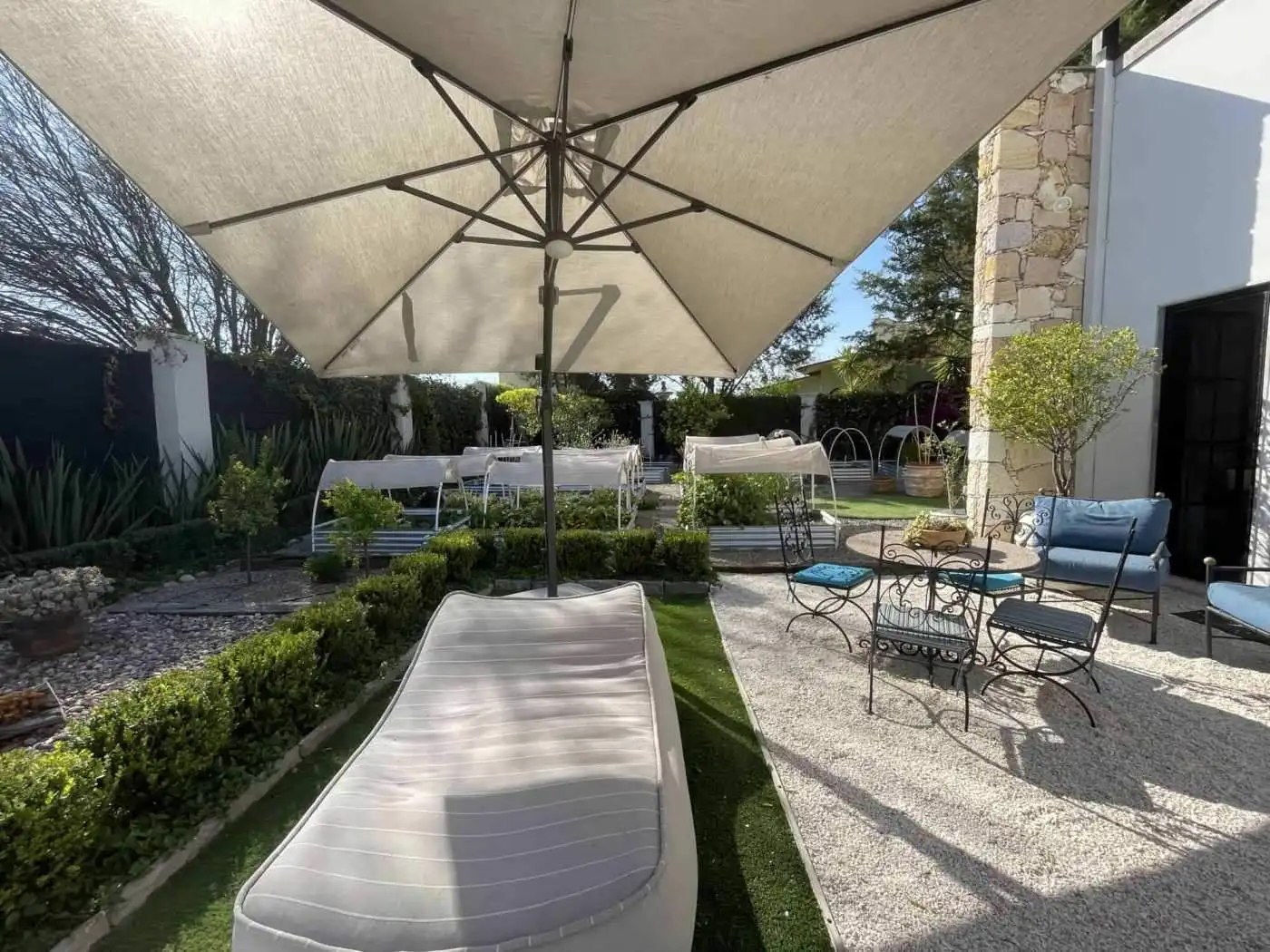 Outdoor patio with sun loungers, table, and chairs in a lush garden setting.