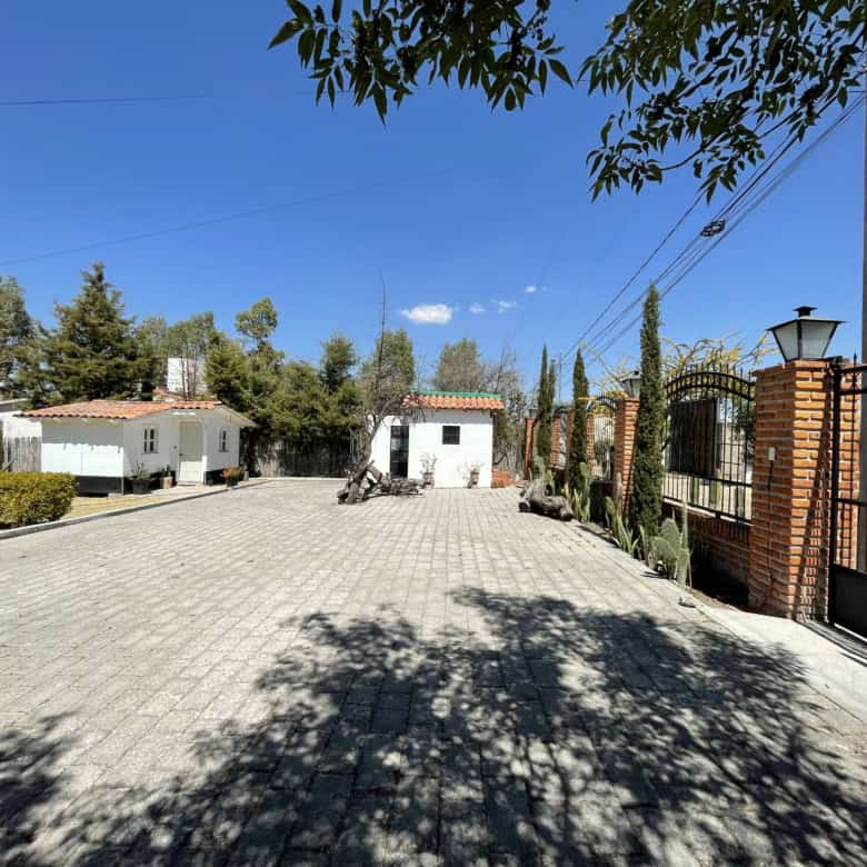 Gated property with paved driveway, trees, and a clear blue sky.