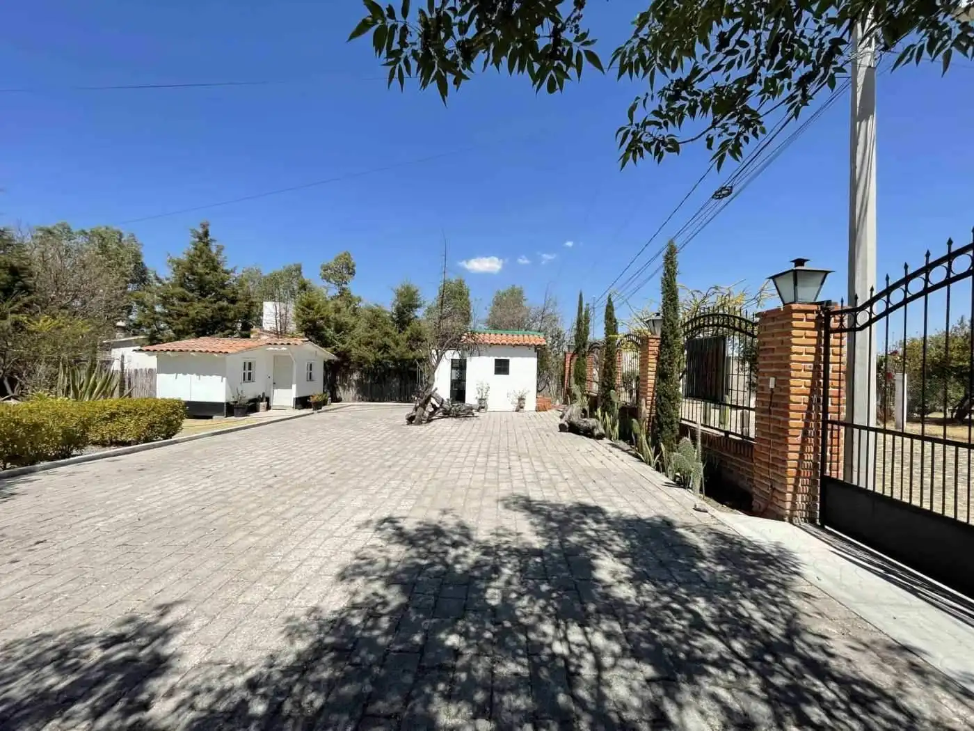 Gated property with paved driveway, trees, and a clear blue sky.