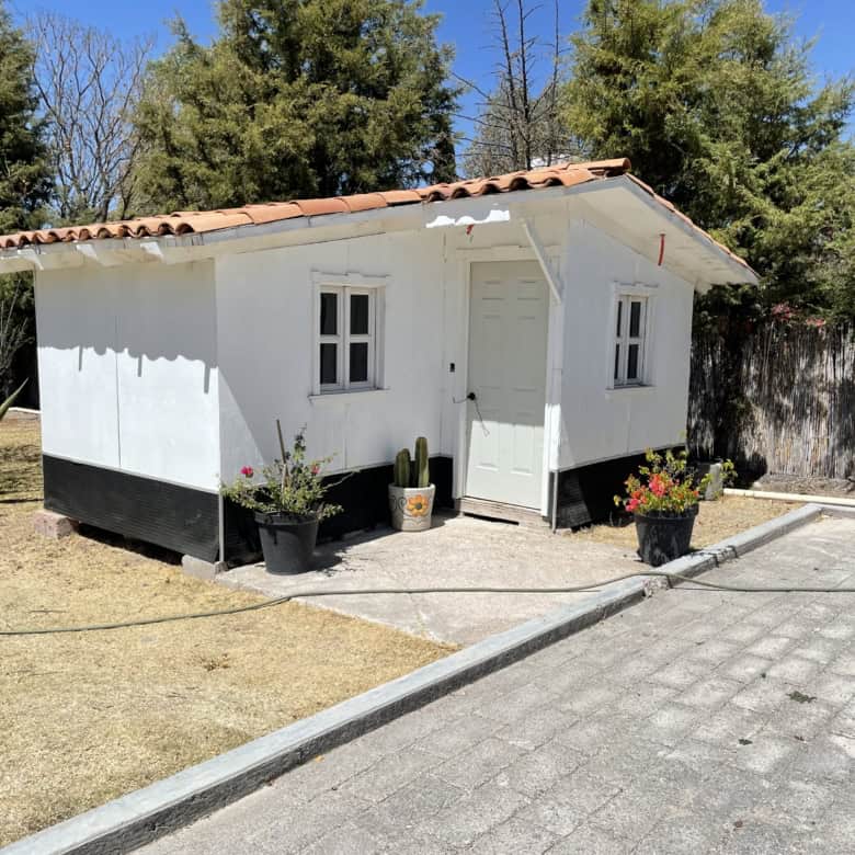 Charming white cottage with garden and potted plants, ideal for a peaceful retreat.