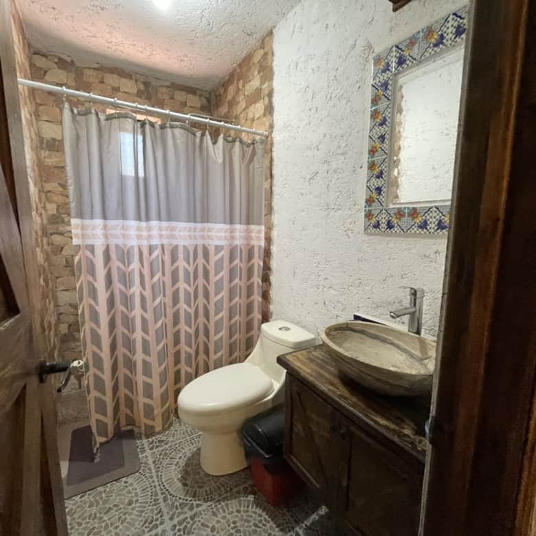Rustic bathroom with stone walls, wooden vanity, and patterned shower curtain.