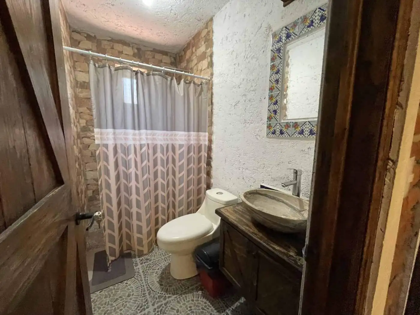 Rustic bathroom with stone walls, wooden vanity, and patterned shower curtain.