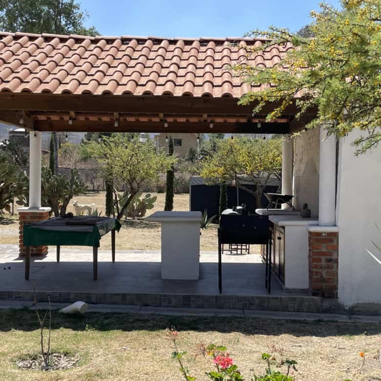Outdoor BBQ and seating area with a tiled roof and garden surroundings.