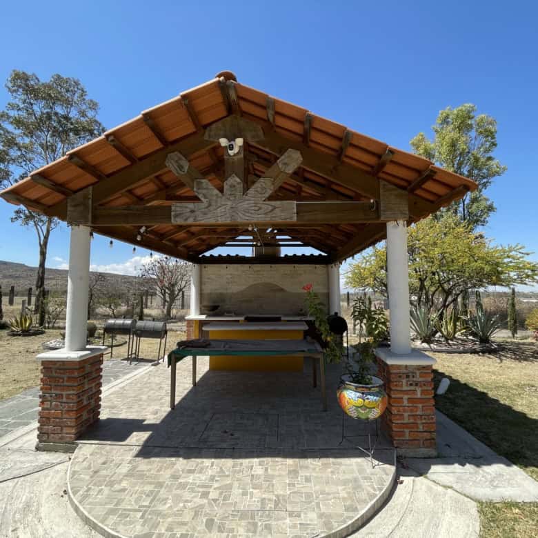 Outdoor BBQ shelter with seating and grill in a peaceful countryside environment.