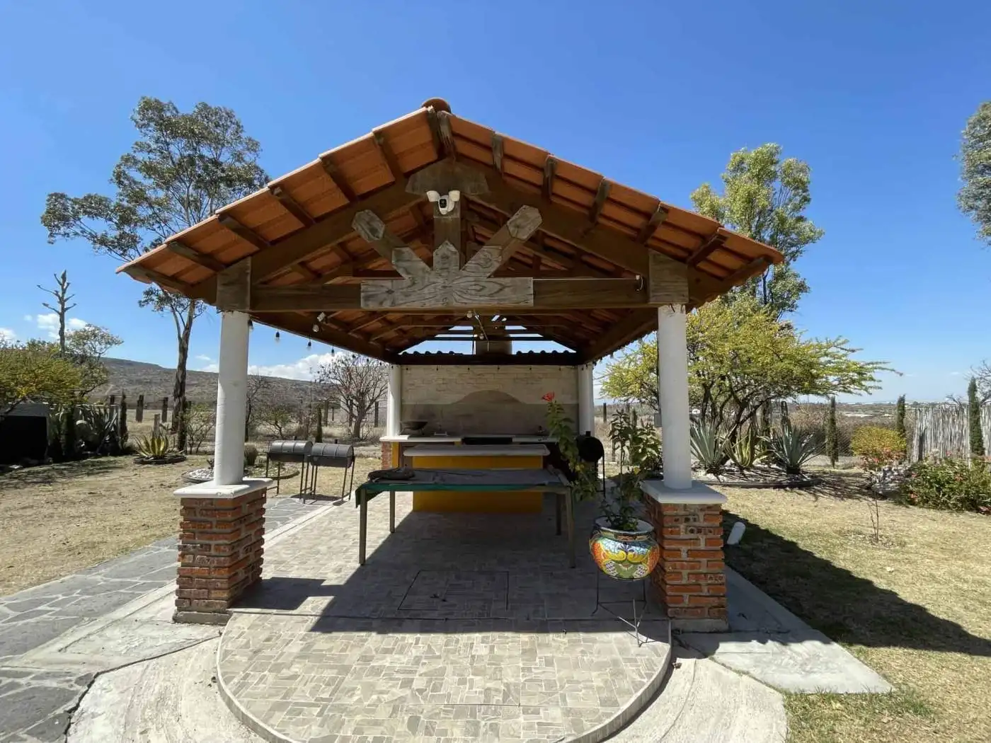 Outdoor BBQ shelter with seating and grill in a peaceful countryside environment.