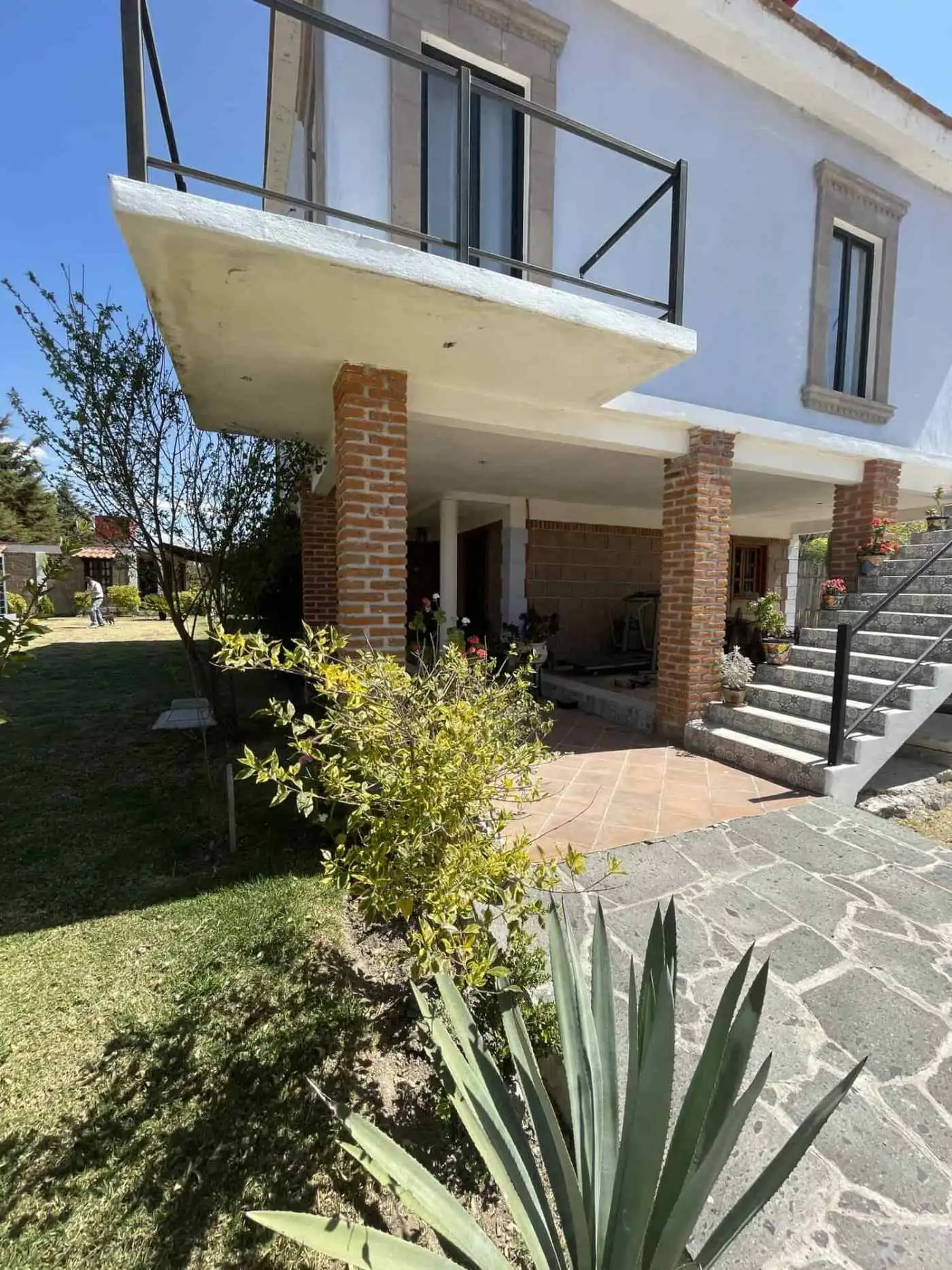 Stylish two-story home featuring a spacious balcony, brick accents, and lush garden surroundings.