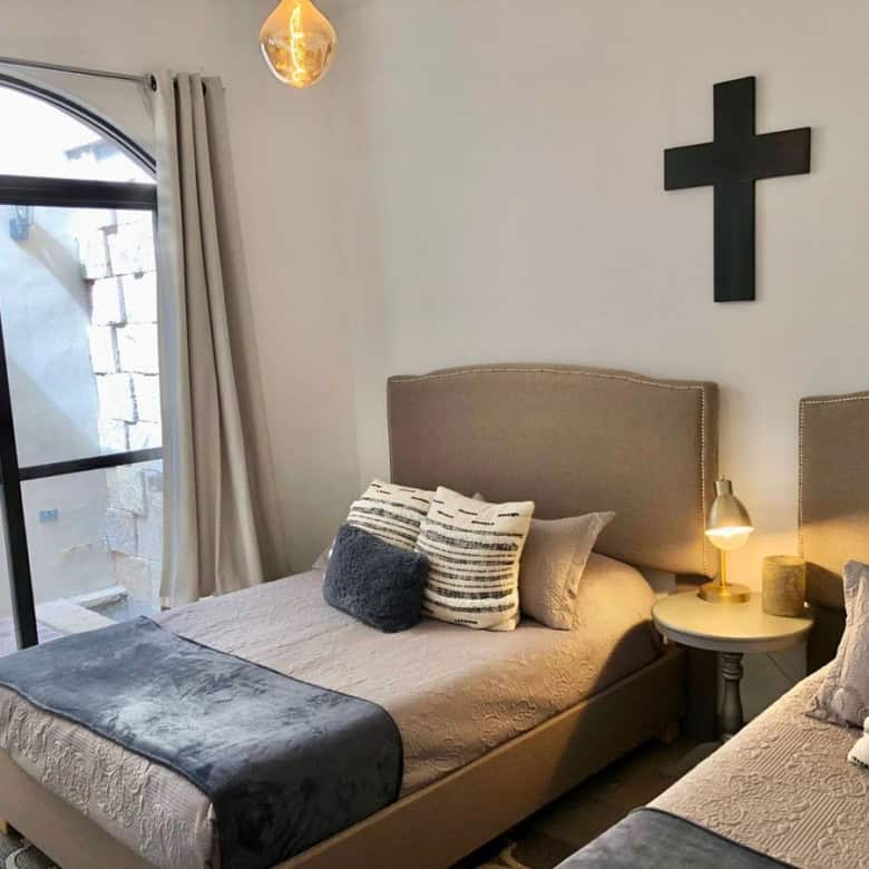 Modern bedroom with two single beds, cross wall decor, and natural light from sliding glass door.