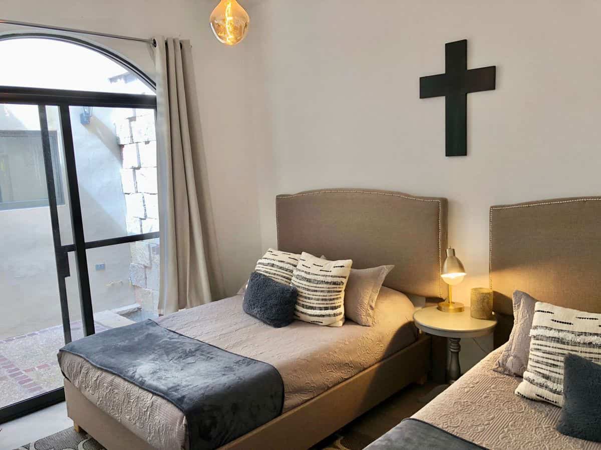 Modern bedroom with two single beds, cross wall decor, and natural light from sliding glass door.
