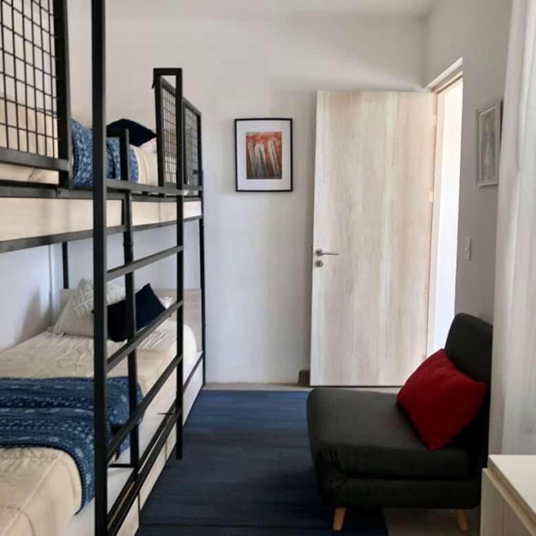 Bunk bed with blue bedding and a small black sofa with red cushion in a bright, minimalist bedroom.
