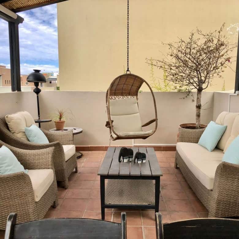 Outdoor terrace with wicker sofas, hanging chair, and potted plants for relaxing outdoor space.