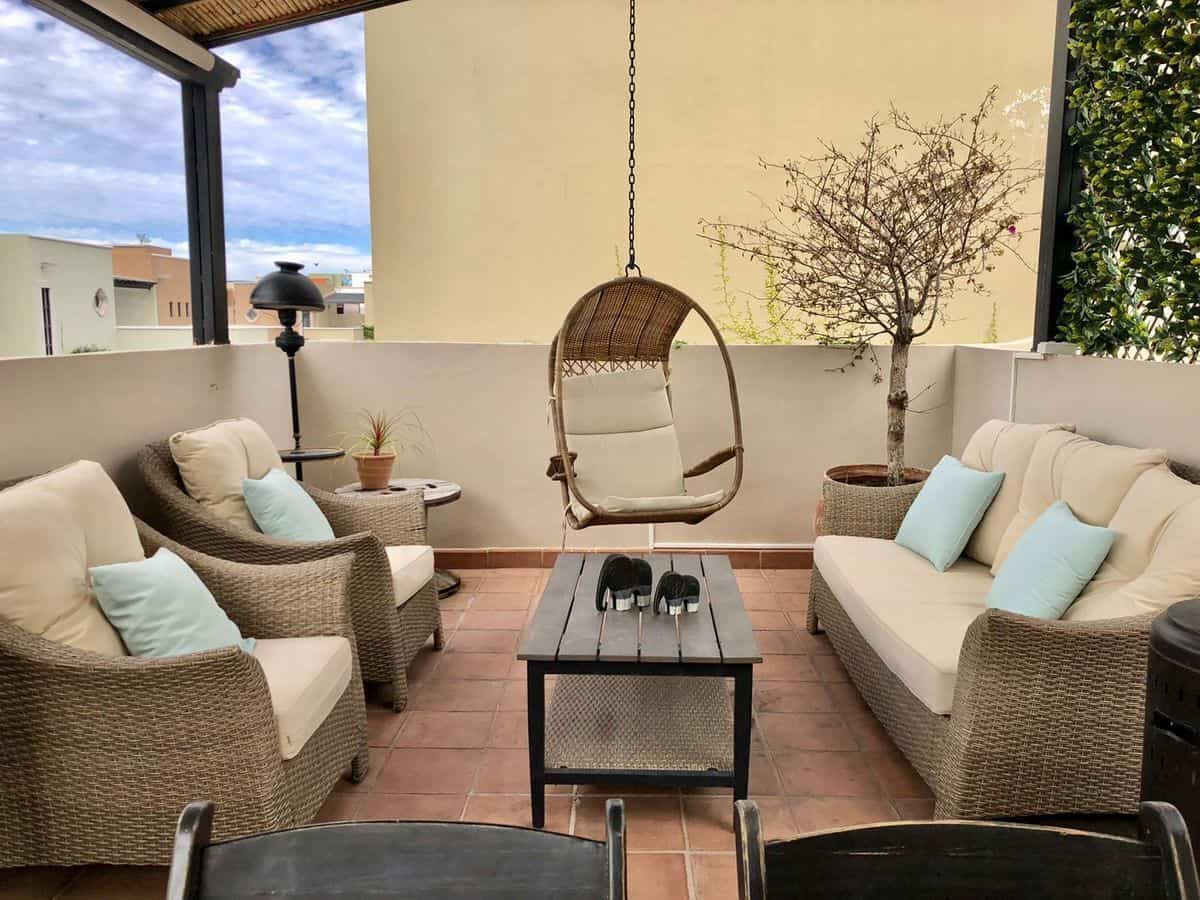 Outdoor terrace with wicker sofas, hanging chair, and potted plants for relaxing outdoor space.