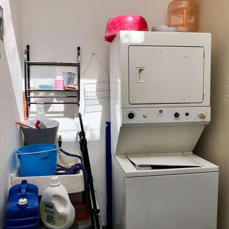 Laundry room featuring a stacked washing machine and dryer with organized shelves and cleaning suppl.