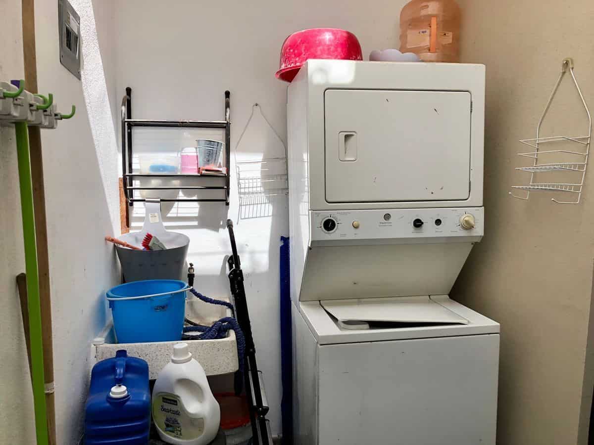 Laundry room featuring a stacked washing machine and dryer with organized shelves and cleaning suppl.