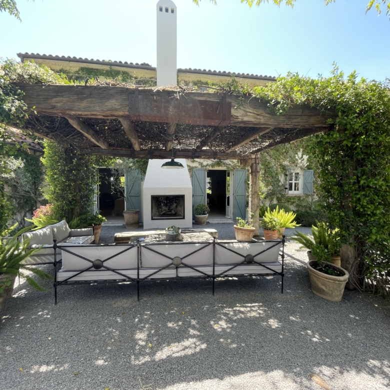 Outdoor patio with fireplace, surrounded by potted plants and greenery.