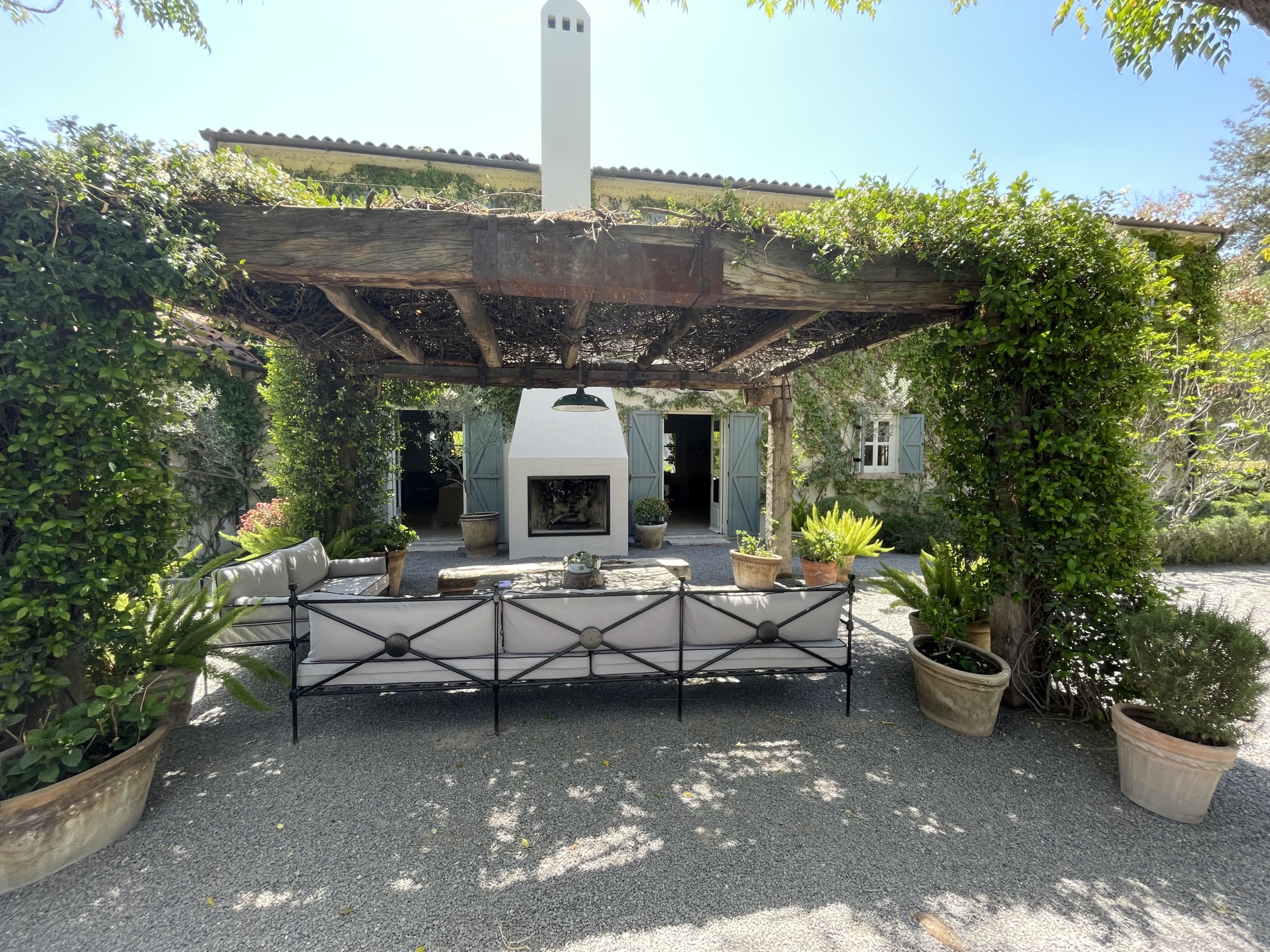 Outdoor patio with fireplace, surrounded by potted plants and greenery.