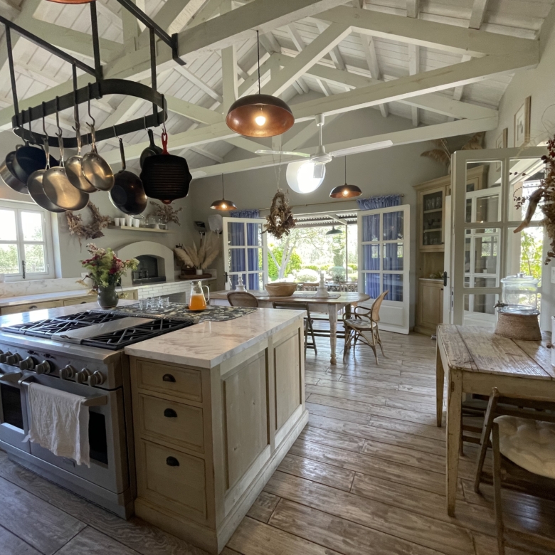 Rustic kitchen with exposed beams, hanging pots, and large windows for bright, airy ambiance.