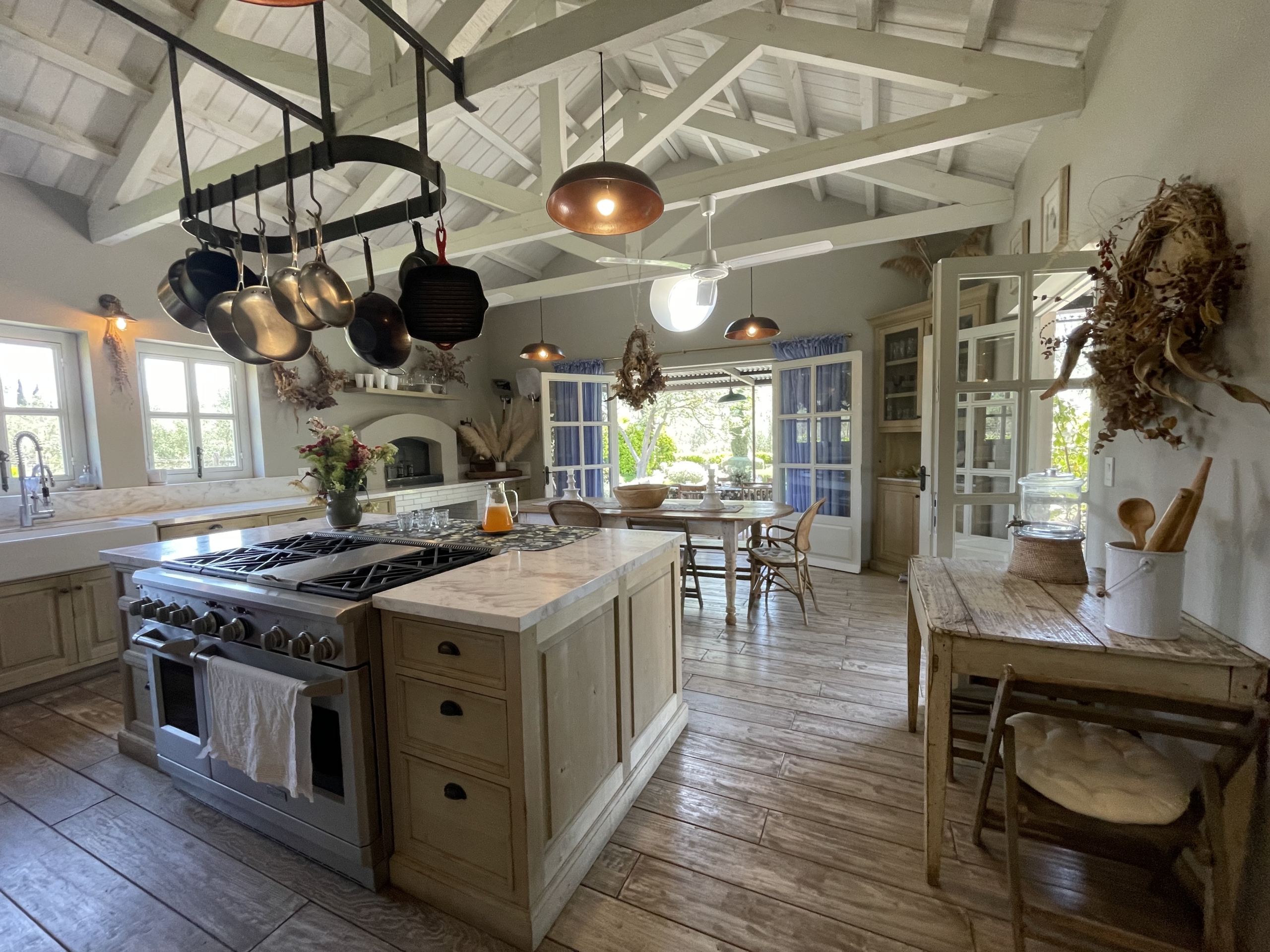 Rustic kitchen with exposed beams, hanging pots, and large windows for bright, airy ambiance.