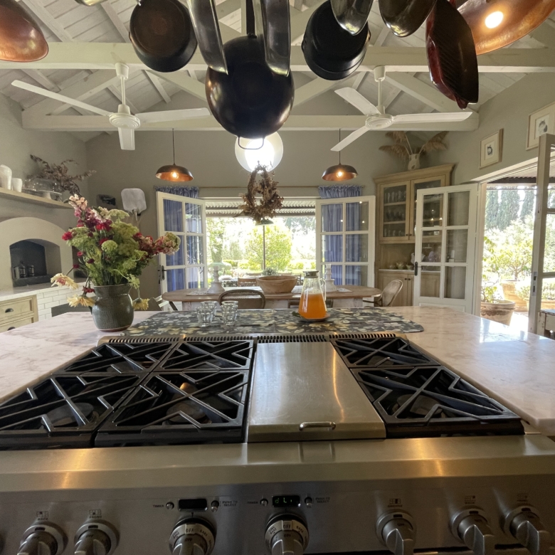 Bright country kitchen with hanging pots, large windows, and rustic decor.