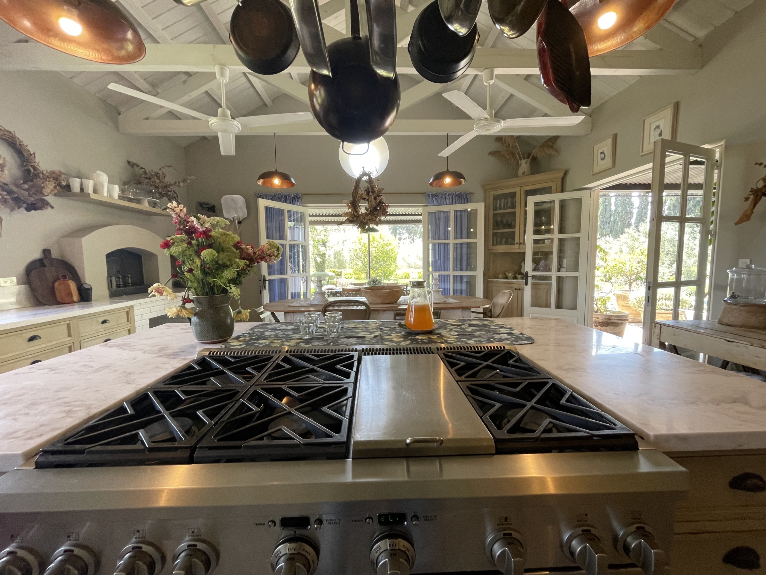 Bright country kitchen with hanging pots, large windows, and rustic decor.