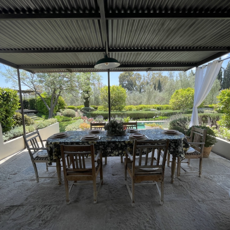 Outdoor dining space with garden and pool view in a sunny, covered patio.