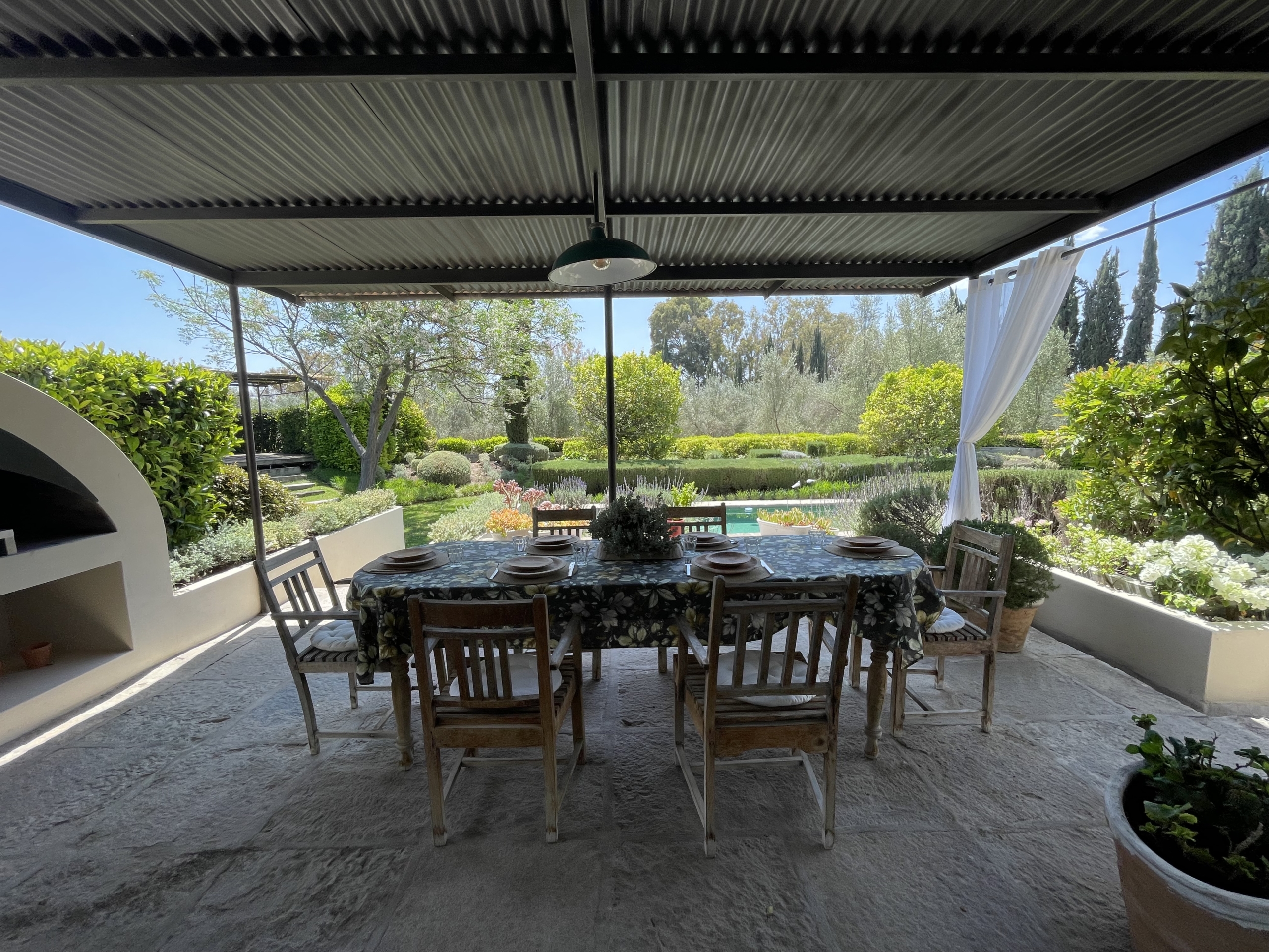 Outdoor dining space with garden and pool view in a sunny, covered patio.
