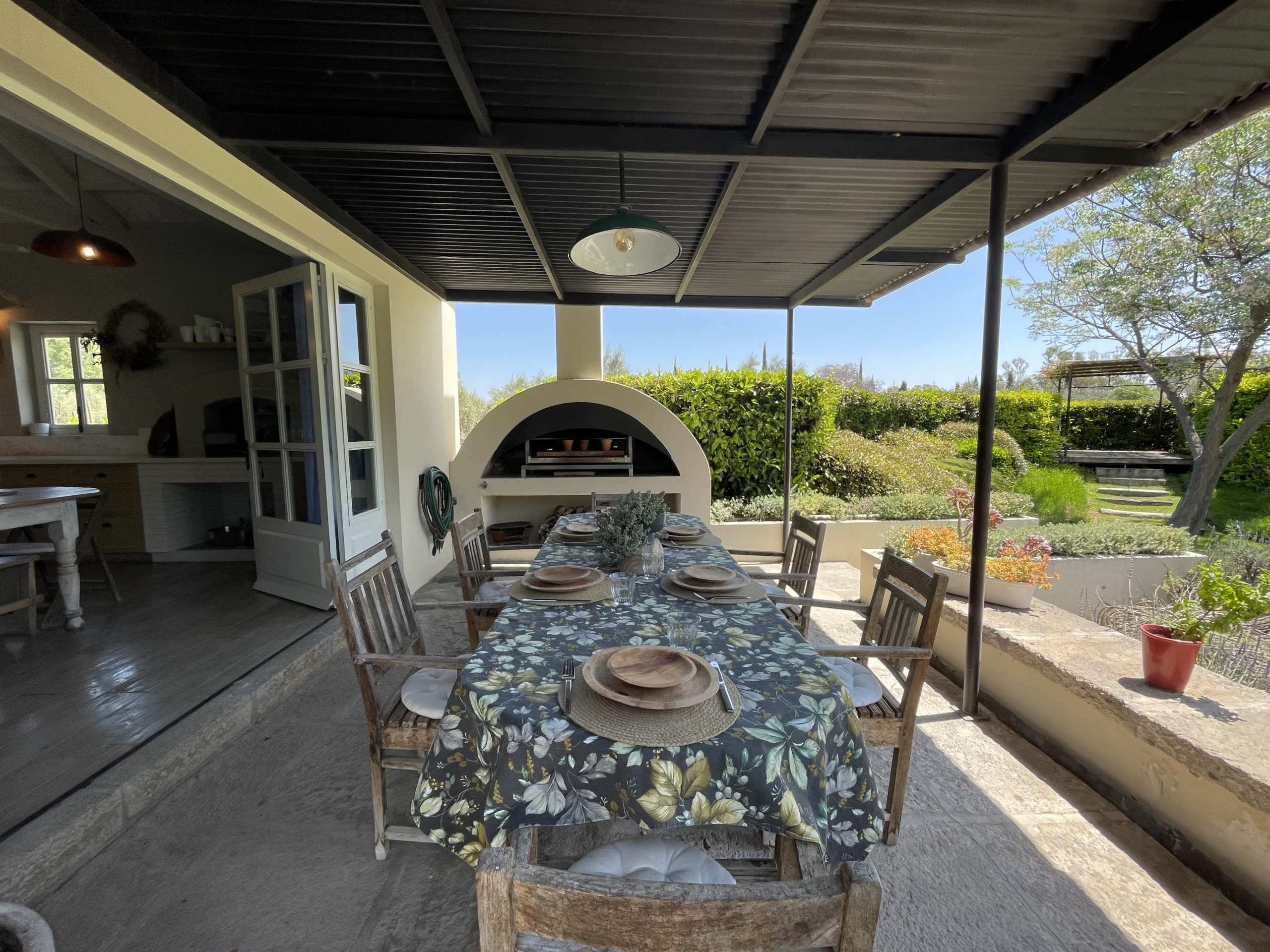 Outdoor dining space with table and chairs under a covered patio, overlooking a lush garden and sunn.