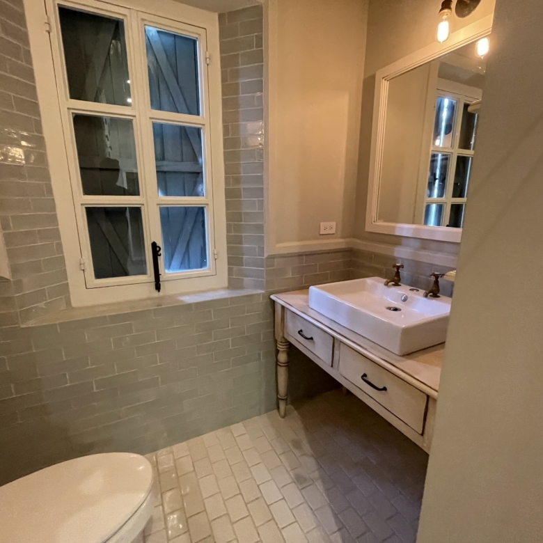 Bright bathroom featuring a vintage sink and mirror, illuminated by warm lighting, with a window pro.