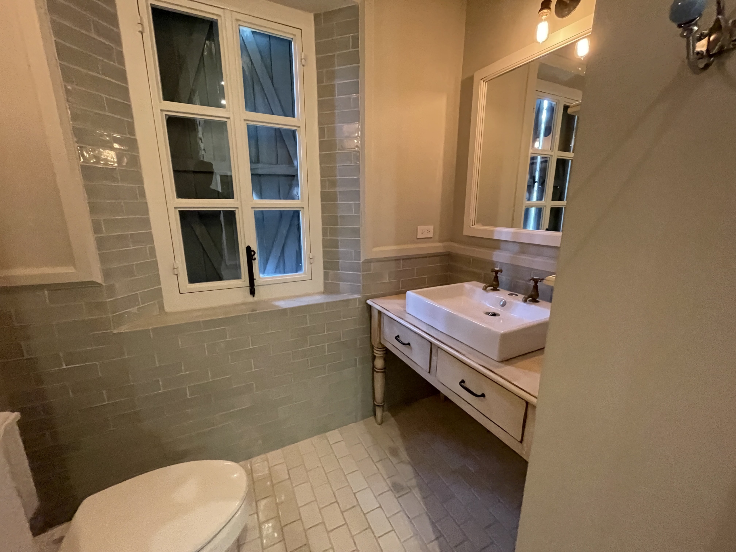 Bright bathroom featuring a vintage sink and mirror, illuminated by warm lighting, with a window pro.