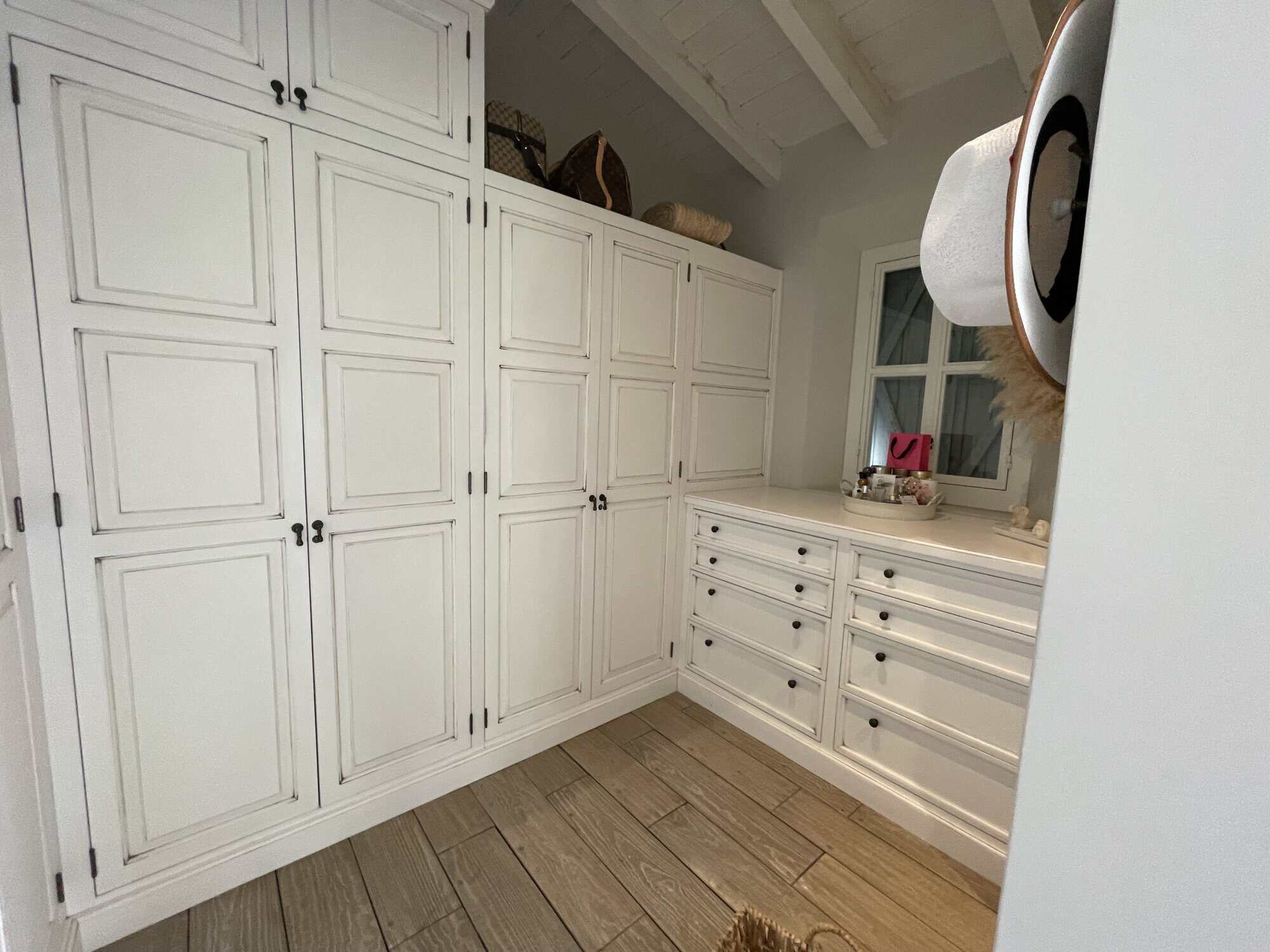 White built-in wardrobe and dresser with ample storage in a bright bedroom setting.