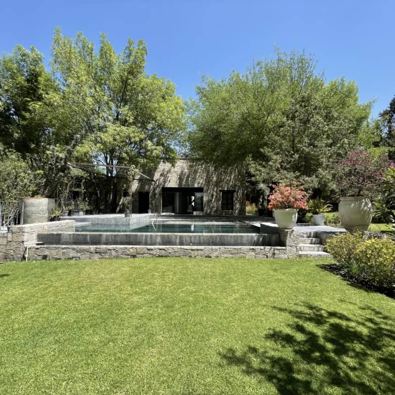 Beautiful garden with a pool, lush trees, and vibrant plants in a serene outdoor setting.
