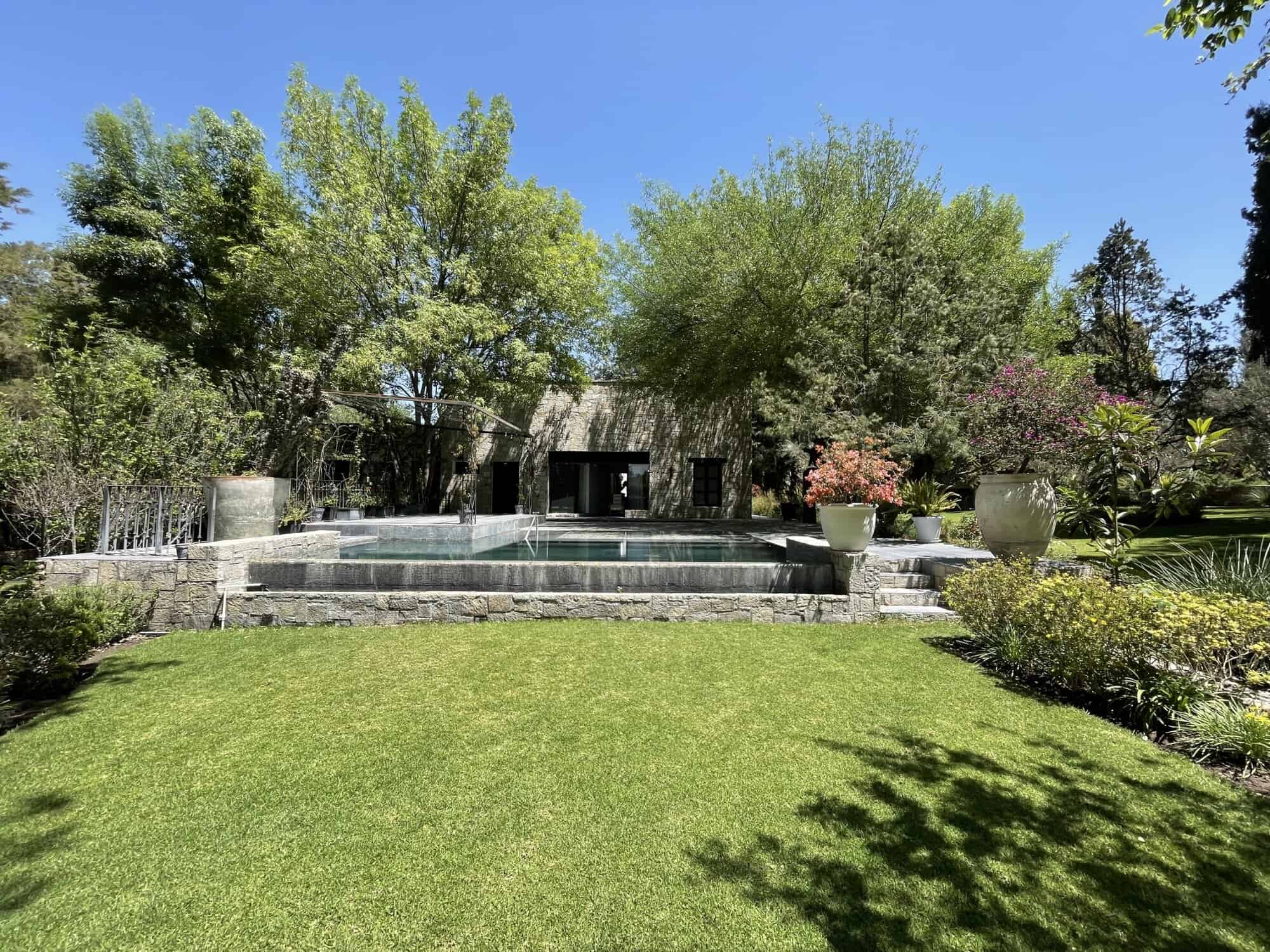 Beautiful garden with a pool, lush trees, and vibrant plants in a serene outdoor setting.