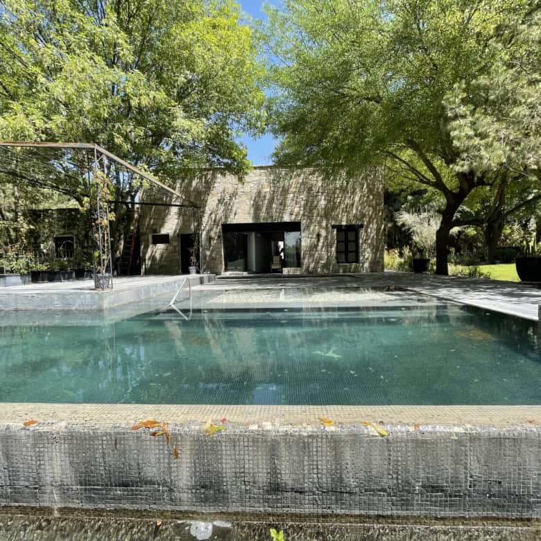 Outdoor pool with surrounding trees and a modern house in the background.