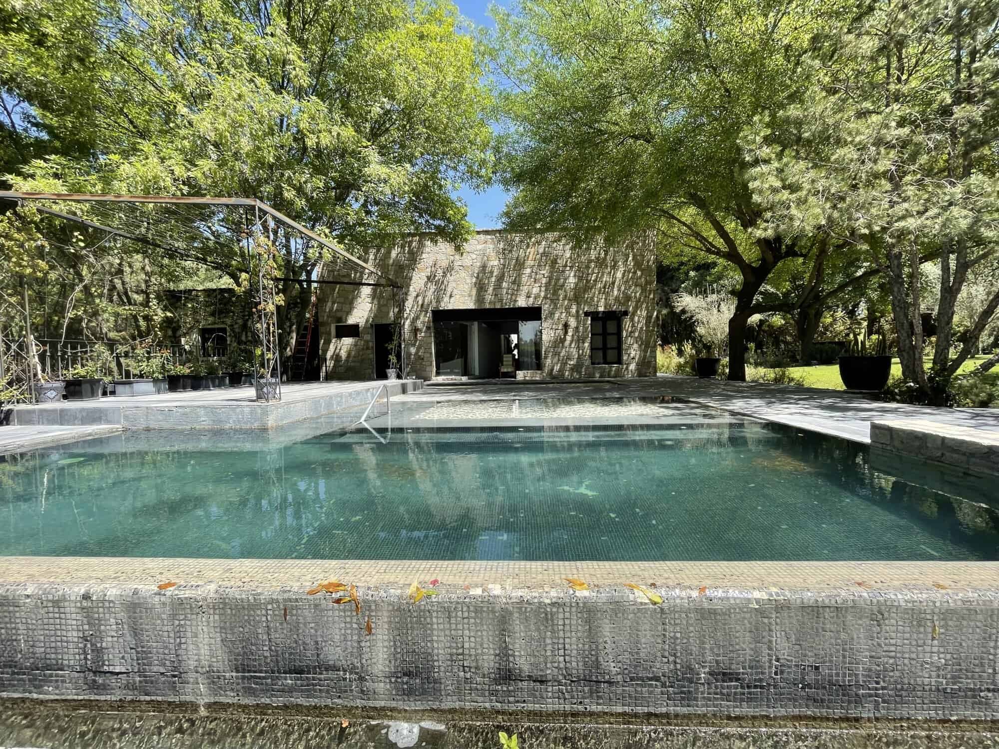 Outdoor pool with surrounding trees and a modern house in the background.