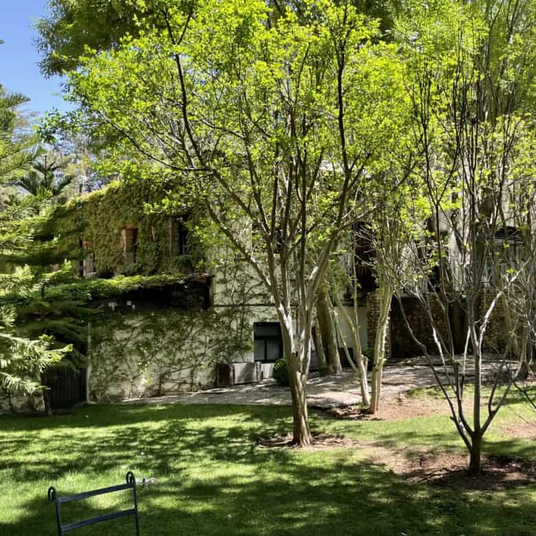 Beautiful garden scene with lush trees and a stone house in the background.