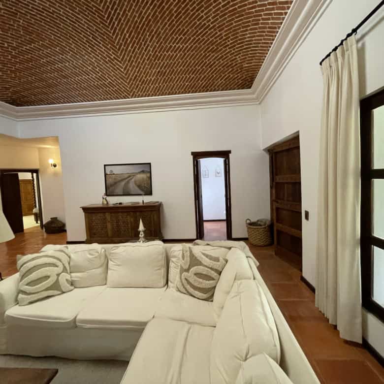 Modern living room with large windows and elegant decor, featuring a white sofa, wooden furniture, a.