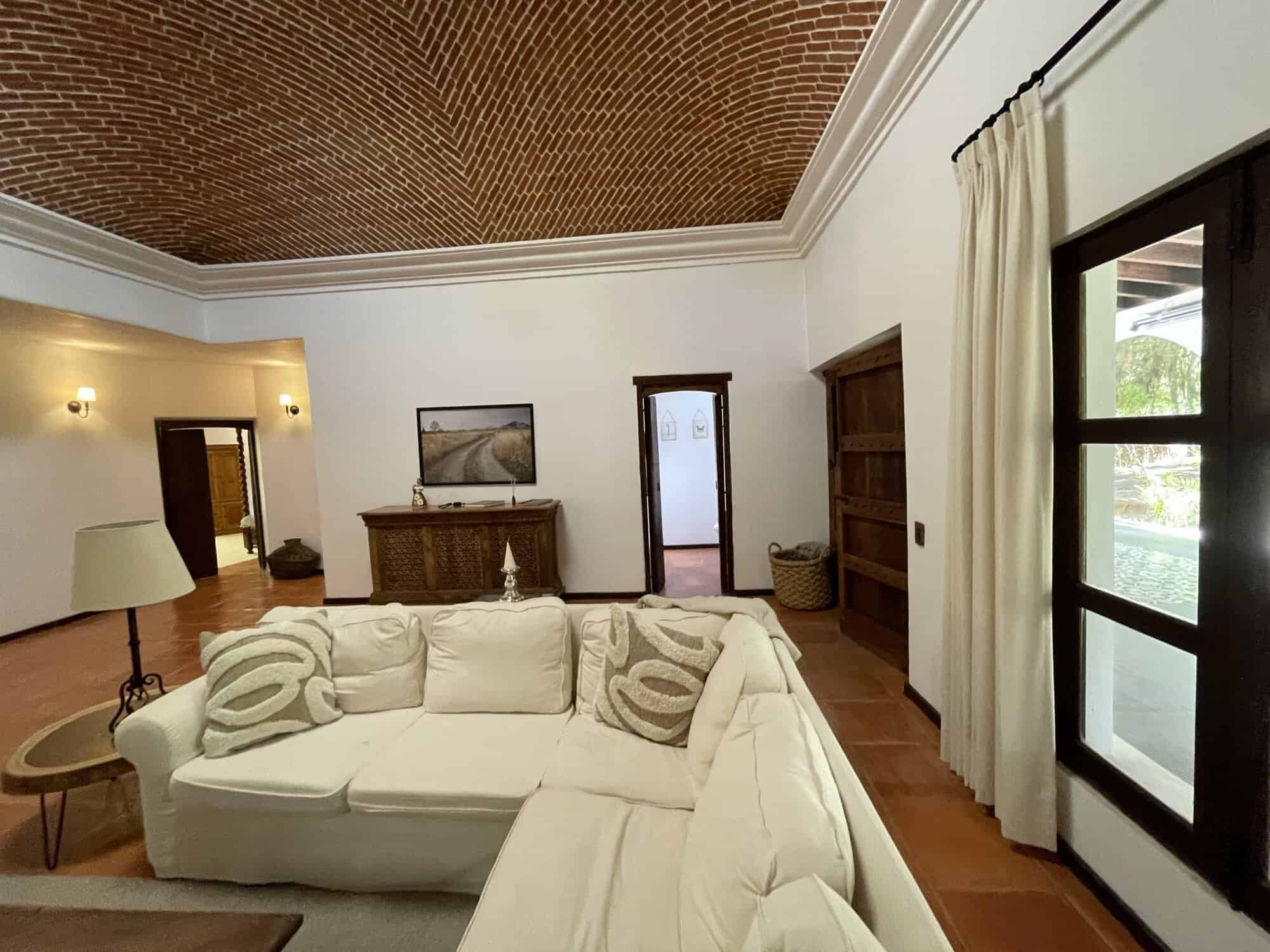 Modern living room with large windows and elegant decor, featuring a white sofa, wooden furniture, a.
