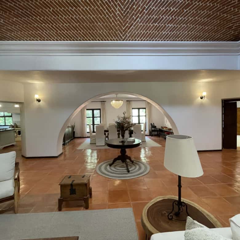Elegant living room with arched doorway and vintage decor, featuring warm lighting, terracotta floor.
