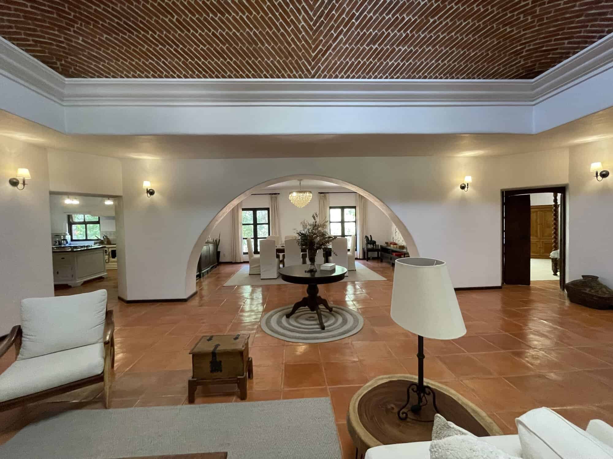 Elegant living room with arched doorway and vintage decor, featuring warm lighting, terracotta floor.