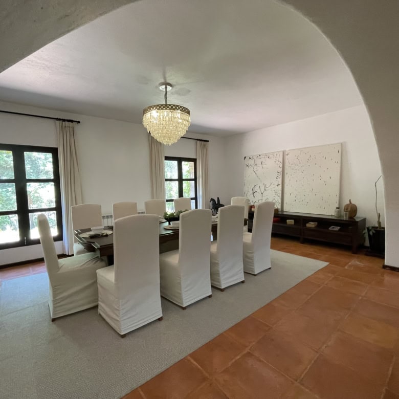 Elegant dining room with white chairs, chandelier, and large windows offering natural light.