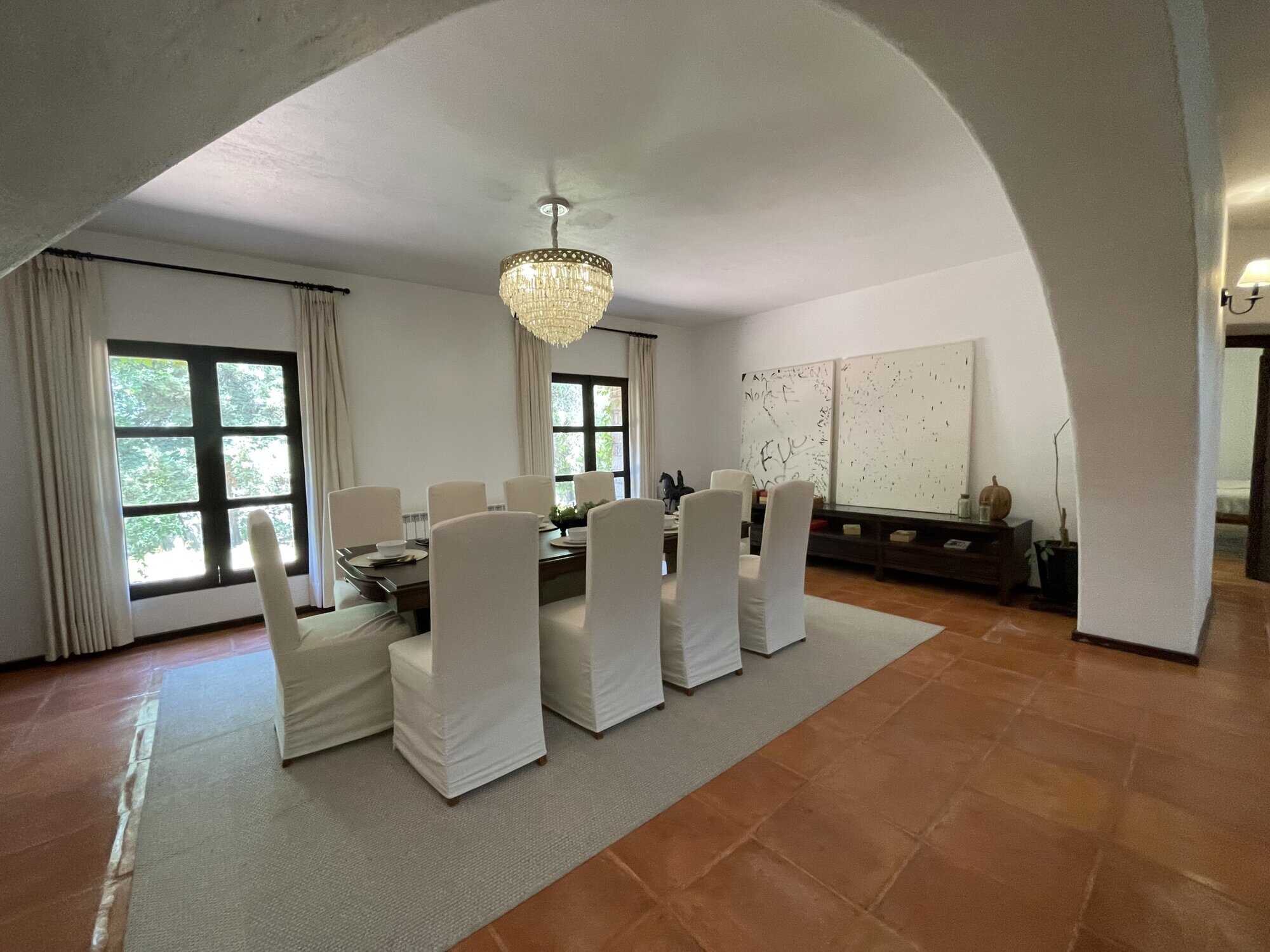Elegant dining room with white chairs, chandelier, and large windows offering natural light.
