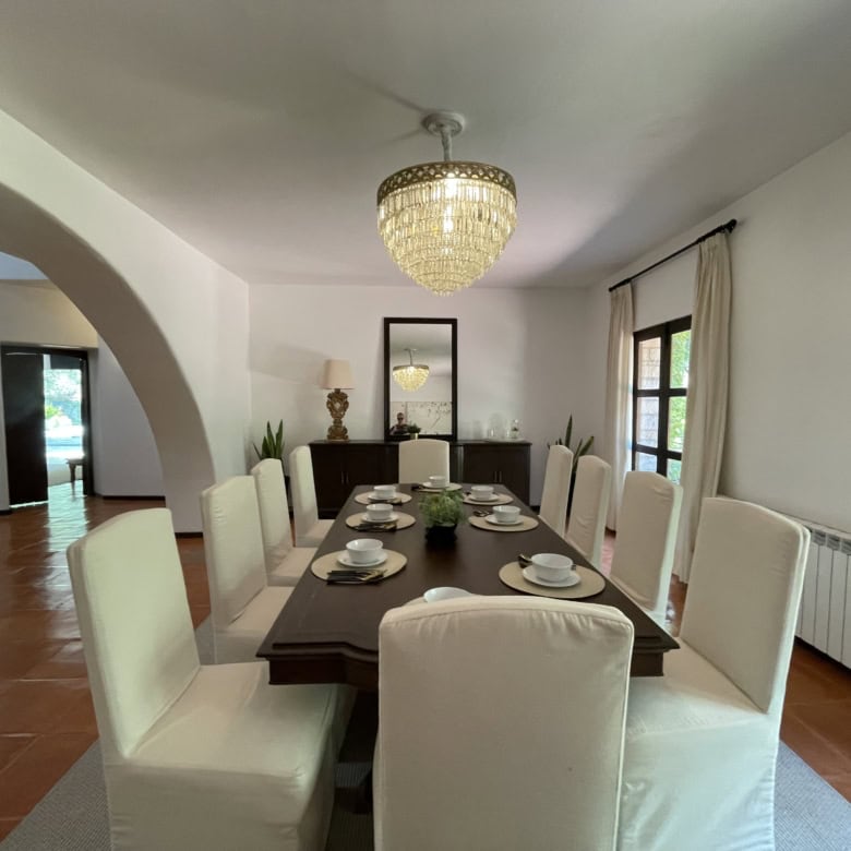 Elegant dining room with white chairs, chandelier, and large windows for a bright, welcoming space.