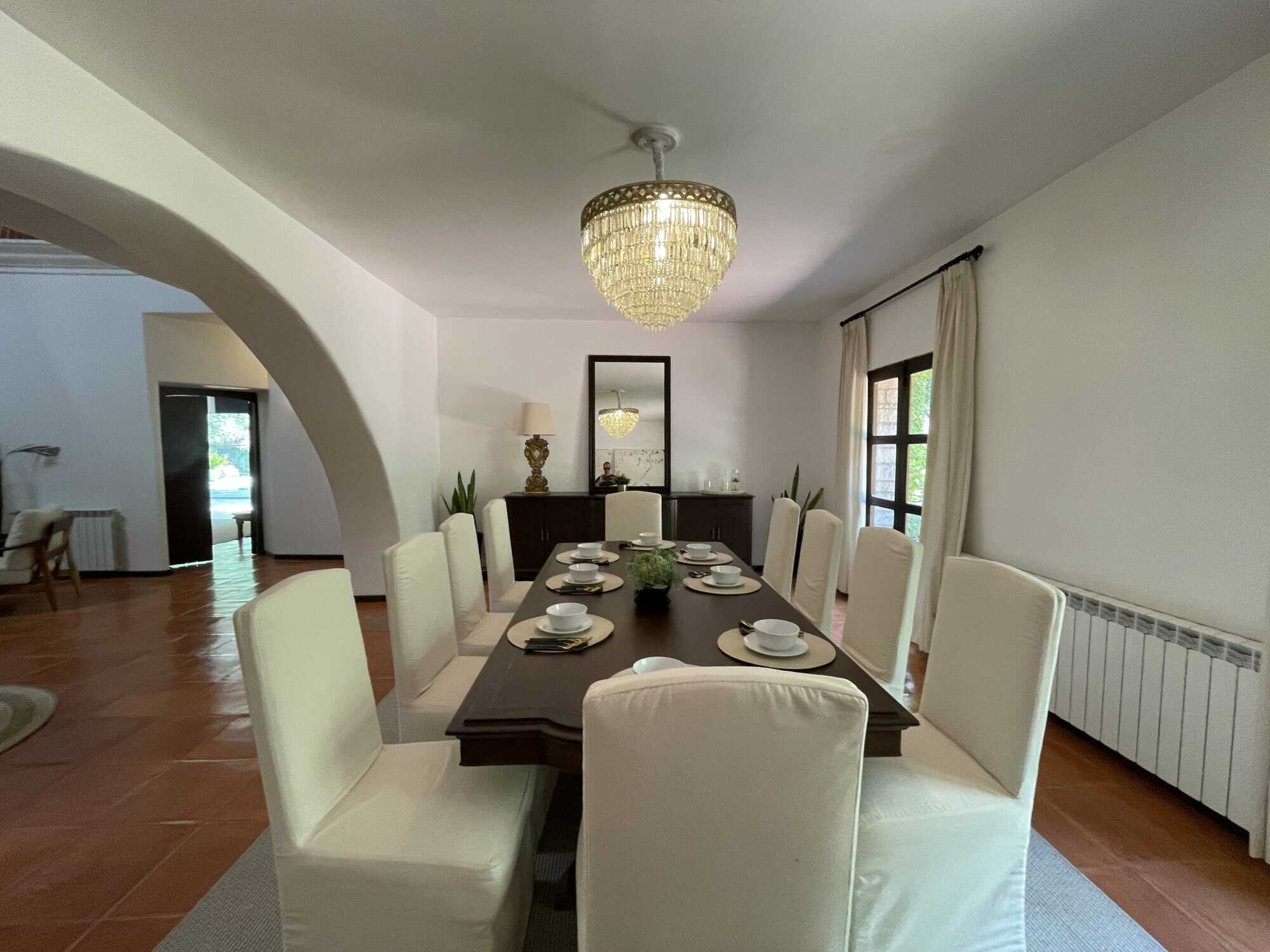 Elegant dining room with white chairs, chandelier, and large windows for a bright, welcoming space.